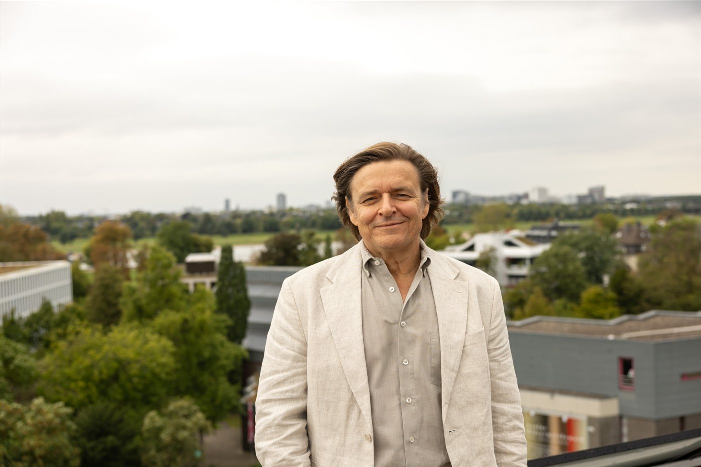 Dr. Ralf Hillemacher im hellen Sakko auf einer Dachterrasse, im Hintergrund eine Stadtlandschaft
